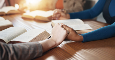 Hand holding, Bible and people with prayer for religion, guidance or support with scripture for worship. Christianity, faith and group by table, book of God and praise with spiritual educationの写真素材