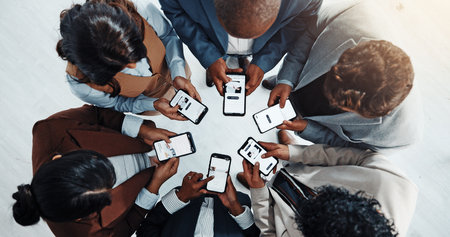 Business people, meeting or huddle with phone in circle above for network or data sync in office. Screen, group or employees browsing with mobile smartphone for information, research or sharing appの写真素材