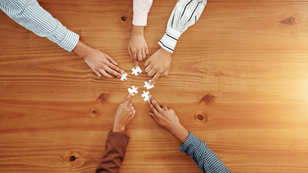 Hands, puzzle and business people in office for partnership, solution or collaboration in meeting. Jigsaw, top view and corporate employees with synergy, problem solving or team building by space.の写真素材