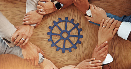 Business people, hands or unity with cog for team building or problem solving together above. Top view, group or employees with wheel mesh or gear in circle for critical thinking or mission on tableの写真素材