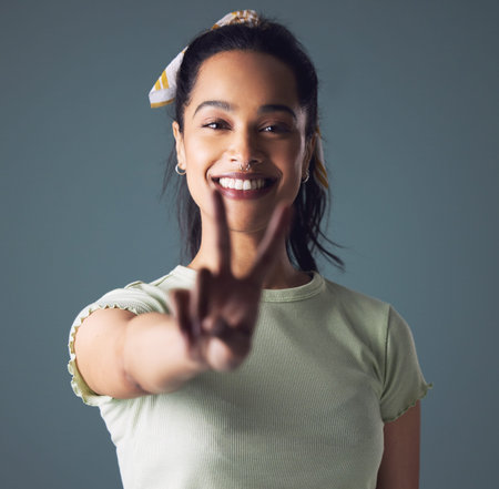 Woman, portrait and peace sign with smile in studio for friendly support, well done or grey background. Female person, face and model with v fingers or emoji gesture for happiness, positive or mockupの写真素材