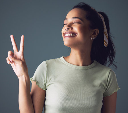 Woman, smile and hand with peace sign in studio for good mood or emoji, grey background or mockup space. Female person, model and happiness or fingers gesture as v joy for relax, wellness or friendlyの写真素材