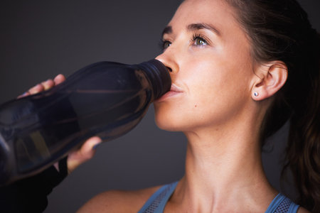 Woman, exercise and drinking water in studio for workout hydration or healthy sports, grey background or training. Female person, bottle and beverage for cardio fitness or liquid, thirsty or breakの写真素材