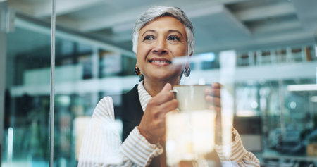 Thinking, coffee break and business woman in office by glass for inspiration, ideas and solution. Professional, corporate and mature worker with beverage for planning, positive mindset and relaxの写真素材