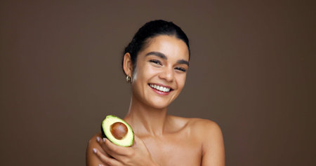 Beauty, woman and portrait with avocado in studio for natural skincare, dermatology or omega 3 on background. Healthy glow, green fruit and sustainable antiaging with clean skin or self care spaceの写真素材