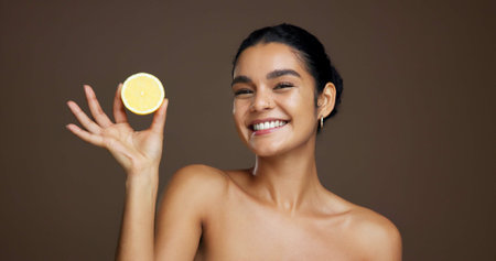Happy woman, portrait or lemon with vitamin C for detox or skincare on a brown studio background. Face, female person or model with smile or natural organic fruit for citrus acid, health and collagenの写真素材