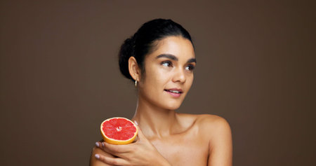 Skincare, beauty and woman with grapefruit, smile and happy for treatment, self care or smooth skin. Studio background, thinking and person with vitamin C for hydration, mockup space and dermatologyの写真素材
