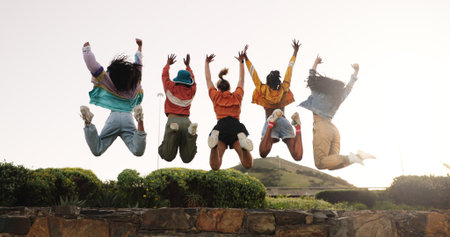 Excited women, friends or fashion with jump in park for achievement, success or freedom together. Back view, female people or happy group in air for winning, excited or celebration in outdoor natureの写真素材