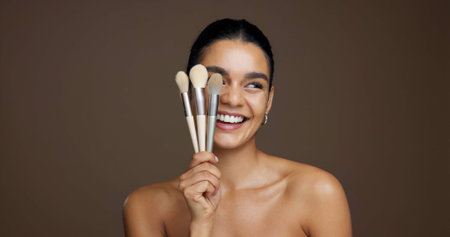 Happy woman, makeup and beauty with brushes in studio for cosmetics on a brown background. Female person, model or smile with product tools for cosmetology, foundation or blending shade on spaceの写真素材