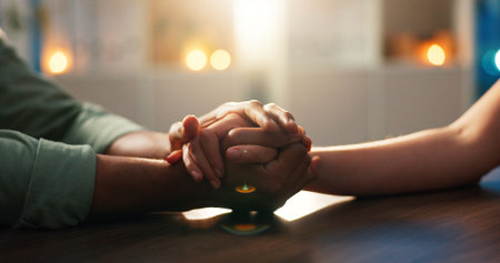 Couple, hands or trust with commitment for love, understanding or comfort on desk in home. Closeup, people and hope together with care, empathy or faith for support, relationship or kindness in houseの写真素材