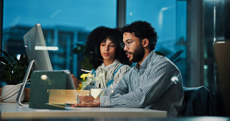 Colleagues, team and collaboration with computer at night, office or journalist with article on web. Reading, research and people with tech for story, creative or working late for project in newsroomの写真素材