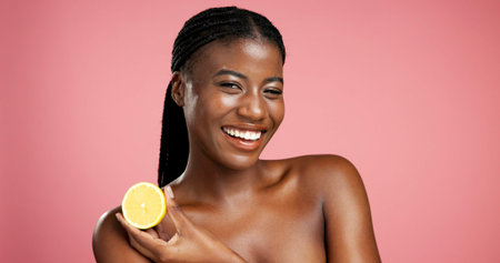 Portrait, black woman and lemon for skincare in studio for vitamin c, brighten skin and natural detox. Female person, citrus fruit and organic benefits, beauty and exfoliate shine on pink backgroundの写真素材