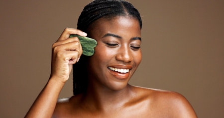 Facial massage, gua sha and smile with black woman on studio space for dermatology or wellness. Beauty, jade stone and skincare with African model on banner to relax skin for antiaging routineの写真素材