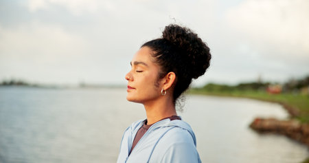 Breathing, fitness and meditation with woman at lake in nature for awareness, balance or wellness. Exercise, eyes closed and zen with calm person outdoor in park for inner peace or mindfulnessの写真素材