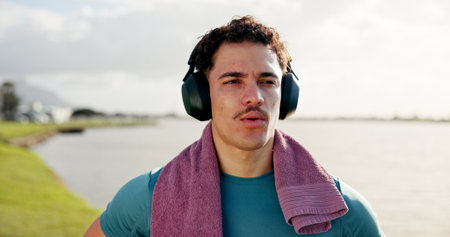 Running, thinking or man in lake with headphones for outdoor training, workout or exercise. Towel, resting and sports athlete on break for streaming radio, music audio or fitness podcast to relaxの写真素材