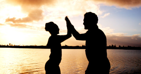 Silhouette, couple and high five with sunset at river for winning, teamwork or success in nature. Active, man or woman with touch for evening activity, achievement or accomplishment together at lakeの写真素材