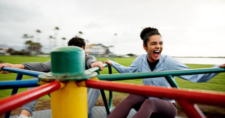 People, laughing and spinning on roundabout at park for workout break, adrenaline or freedom. Fitness, excited or couple with energy on carousel on playground for playing together or rest from cardioの写真素材