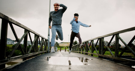 Exercise, running and couple with jumping on bridge for pace training, winter workout and teamwork. Fitness, puddle and people with cardio outdoor for race endurance, marathon competition and supportの写真素材