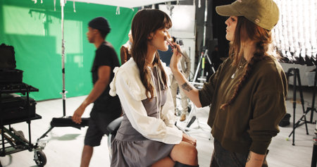 Set, women and makeup artist with brush, beauty and application of cosmetics, creative and makeover. Behind the scene, people and getting ready for photoshoot, preparation and crew with equipmentの写真素材