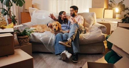 Couple, dog and talking on sofa in new house for interior design, decoration ideas and planning. Night, people and happy with discussion in first home for renovation, property investment or moving inの写真素材