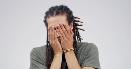 Embarrassed, news and worry with hands on man in studio for debt crisis, challenge and gambling addict. Lottery mistake, mental health and finance loss with person on white background space for failの写真素材