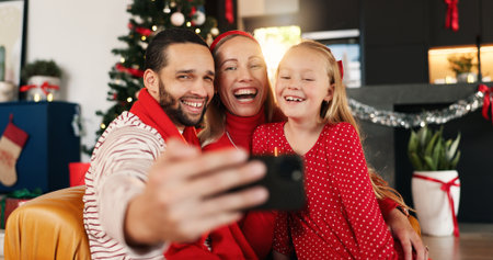 Christmas, selfie and smile of family in living room of home together for celebration or memories. App, excited or photograph with dad, daughter and mom in apartment for festive profile pictureの写真素材
