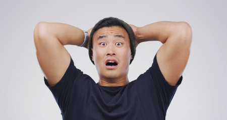 Portrait, Asian man and mind blown in studio for fake news, bad rumor and gossip drama. Male person, space and shocked reaction for horror story, danger risk and revelation secret on white backgroundの写真素材