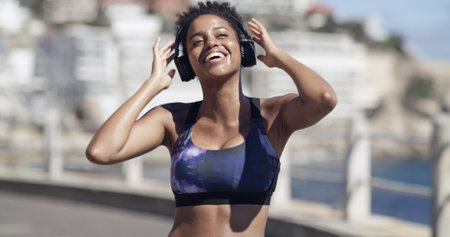 Smile, woman and headphones for fitness in city for audio, listening to music and exercise podcast. African person, streaming and good mood, workout playlist and sports training of marathon practiceの写真素材