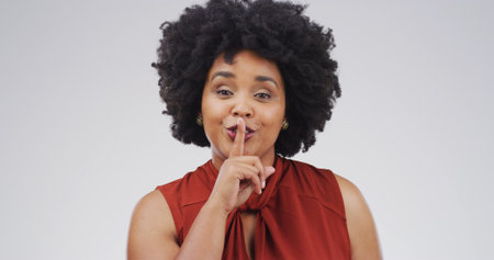 Portrait, woman and quiet in studio to stop noise or gossip on white background space. Silent, secret or African person with finger on lips for privacy, confidential news or shush sign for conspiracyの写真素材