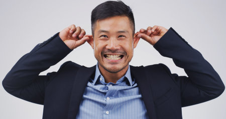 Funny face, ears and portrait of asian man in studio for comic, meme and joke. Facial expression, comedy and happiness with person on white background space for good mood, goofy and silly emojiの写真素材