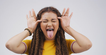 Girl, funny face and playful with tongue out in studio, eyes closed and mock up space on white background. Gen z woman, comic expression and silly with mouth, laugh or humor with quirky emojiの写真素材