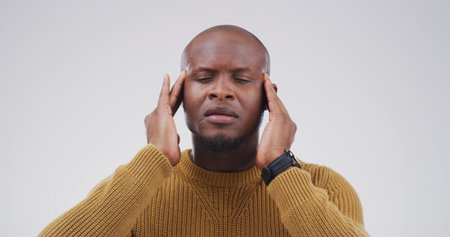 Stress, migraine and black man in studio with pain, brain fog and fibromyalgia on white background. Headache, tired and sick person with mental health crisis, burnout and massage temples for reliefの写真素材