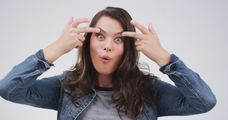 Crazy, funny face and portrait of woman in studio with open eyes, silly and comic facial expression. Goofy, joke and female person from Canada with comedy gesture for humor by white background.の写真素材