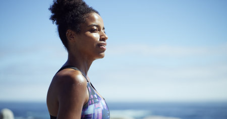 Black woman, fitness and break at beach, promenade or thinking with space, sky and smile. African runner, girl and reflection with profile for workout, training or ocean for perspective in Nigeriaの写真素材