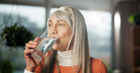Home, senior woman and drinking water for health, nutrition or wellness benefits. Glass, hydration and elderly person with liquid for detox, diet and natural beverage with electrolytes in retirementの写真素材