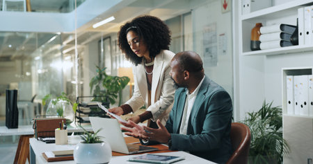 Document, business people and team brainstorming in office for insurance, meeting or idea at night. Laptop, collaboration and African workers planning, risk assessment or help with policy on overtimeの写真素材