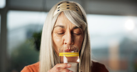 Lemon, water and mature woman in home with drink for detox, antioxidant and vitamin c in morning. Glass, diet and person with liquid, citrus fruit and minerals for digestion, wellness and nutritionの写真素材