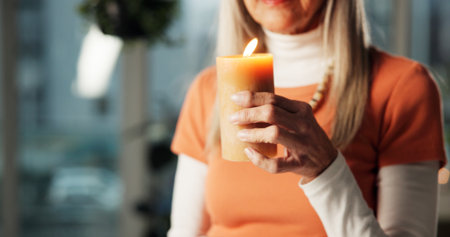 Woman, hands and candle in home for aromatherapy, zen or scented wax for ambience with wellness. Atmosphere, light and senior person with flame for peace, calm or relax with holistic healing at nightの写真素材