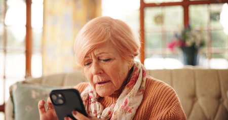 Senior woman, reading and phone at house for message, communication and social media. Elderly person, confused and mobile with online games, browsing website and problem solving of crossword activityの写真素材
