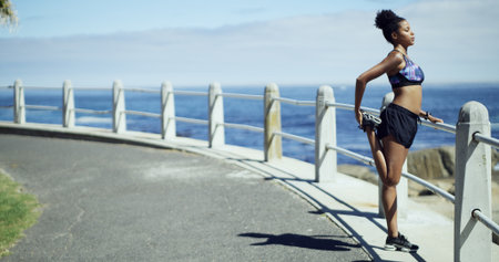 Black woman, exercise and stretching legs at beach promenade, ready or thinking for fitness. African runner, girl and reflection with profile for workout, training or ocean with warm up in Nigeriaの写真素材