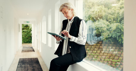 Mature woman, reading and tablet at house for research, email client and selling property. Female realtor, digital and website for real estate sales, review information and schedule viewing of rentalの写真素材