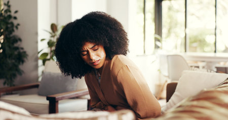 Woman, stomach and cramps or pain on sofa for menstruation, ovarian cysts and discomfort in lounge. Girl, home and abdominal ache for monthly cycle, period and tension or strain in house living roomの写真素材