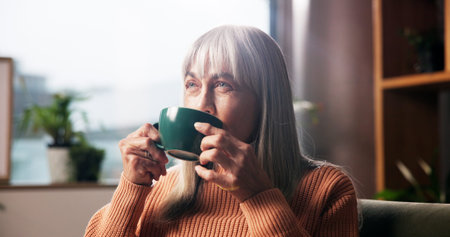 Senior woman, drinking coffee and thinking on sofa with nostalgic memory, daydreaming or wondering....
