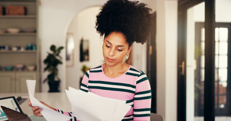 Woman, paperwork and remote work from home with review, finance and info for tax compliance, African person, documents and freelancer with administration, feedback or budget report at apartmentの写真素材