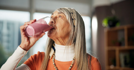 Smoothie, drinking and mature woman in home for gut health, benefits and wellness in morning. Kitchen, diet and person with protein shake, cocktail and beverage for digestion, nutrition and detoxの写真素材