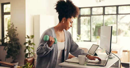 Multitasking, freelancer and woman with dumbbell, computer or standing desk for project or exercise. Research, journalist and African person with equipment for workout, remote work or fitness in homeの写真素材