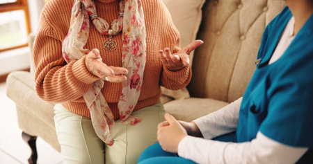 Hands, nurse and senior person on sofa with conversation, healthcare assessment and support in retirement. People, caregiver and elderly patient on couch, consultation and explain symptoms in houseの写真素材