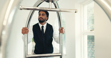 Porter, service and push trolley in hotel for luggage handling, check in welcome and guest arrival. Employee, hospitality and man with cart at luxury resort for bellboy assistance, concierge and helpの写真素材