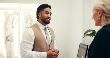 Hotel, concierge and man with customer at front desk for reservation, booking room and check in. Hospitality, receptionist and person with woman talking for help, service and accommodation infoの写真素材