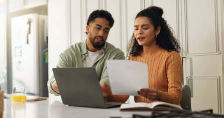Laptop, documents and research with couple in kitchen for bills, home loan and financial planning. Online banking, paperwork and budget review with man and woman reading in house for applicationの写真素材